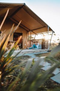 Luxury Glamping Paar beim Entspannen auf der Terrasse mit Sonnenuntergang vorm Safari Zelt